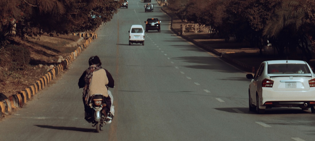 Cars and a motorcycle driving down a road in Pakistan